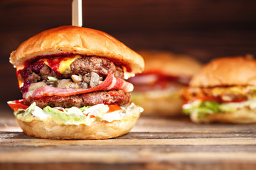 Close-up of home made tasty burgers with beef, mushrooms, bacon, and cheese on wooden table. cranberry hot sauce. one in the foreground and in the background two more