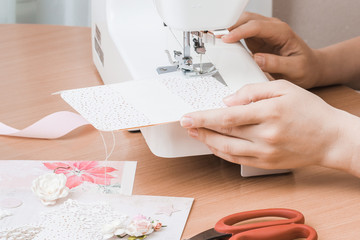 Female hands working for the white sewing machine. Scrapbooking for wedding or other festive decorations .
