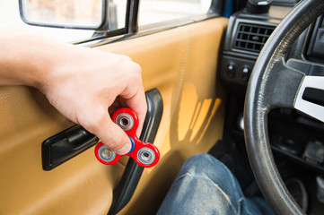 Close-up of a man's hand playing with a spinner while in a traffic jam on the background of the car's interior