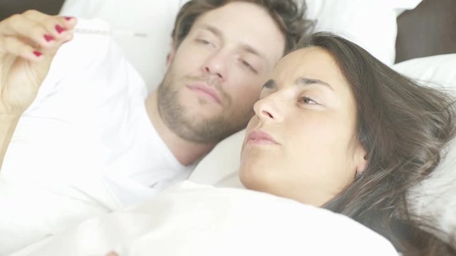 Woman lying in bed taking temperature with thermometer
