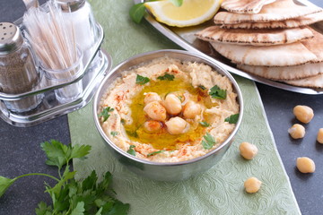 Chickpea paste with chick peas, garlic, cumin, sesami seads, olive oil, coriander in a metal bowl on a green cloth with pita bread and parsley. Traditional food. Healthy eating concept