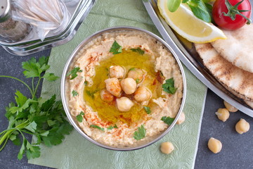 Chickpea paste with chick peas, garlic, cumin, sesami seads, olive oil, coriander in a metal bowl on a green cloth with pita bread and parsley. Traditional food. Healthy eating concept