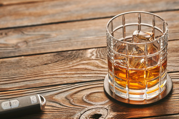 Glass of whiskey or alcohol drink with ice cubes and car key. Drink and drive concept.