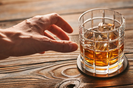 Man's hand reaching to glass of whiskey with ice cubes. Alcoholism concept.