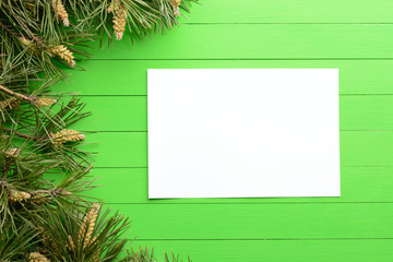 A blank piece of paper among pine branches on a green wooden background