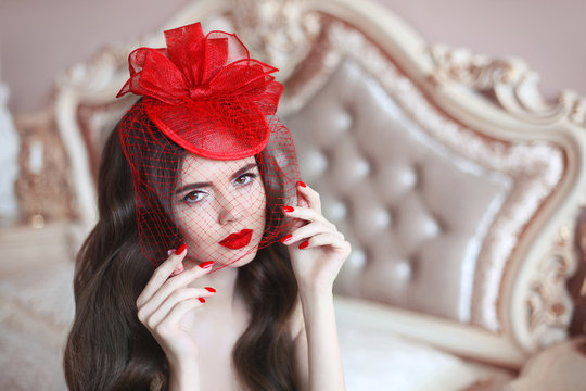 Elegant woman in retro hat with red lips and manicured nails. Brunette closeup portrait. Sensual female posing in luxury modern bedroom interior.