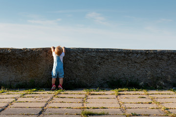 The little girl tries to see what's behind the wall.