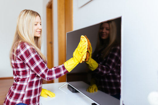Beautiful young smiling woman cleaning TV with microfiber cloth.