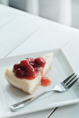 A piece of cherry cheesecake on white wooden table