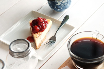 A piece of cherry cheesecake and black coffee on white wooden table