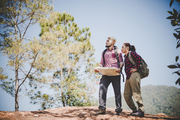 Young couple with backpacks looking at map during hiking in the mountain.