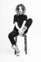 Fototapeta premium A smart girl is sitting on a chair in a fashionable suit. Black white photo of a girl.