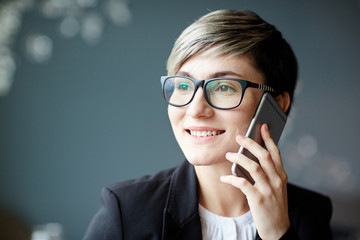 Pretty young businesswoman with cellphone talking to client