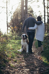 Young couple enjoying nature outdoors together with their Saint Bernard puppy. 