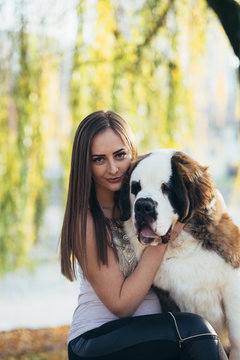 Beautiful young brunette woman with her adorable Saint Bernard puppy in park. 