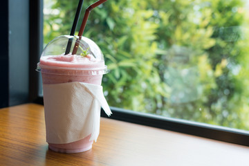 A glass of strawberry smoothie on wooden table with green view