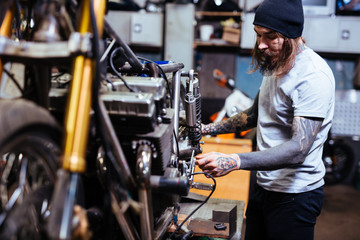 Side view portrait of bearded tattooed mechanic  working in garage customizing  motorcycle and...