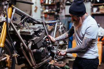Portrait of focused tattooed man working in garage customizing motorcycle and repairing broken parts