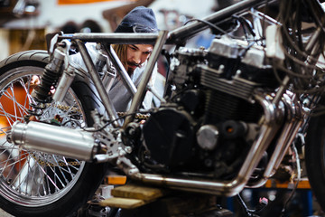 Fototapeta na wymiar Portrait of bearded long-haired man working in garage customizing motorcycle and repairing broken parts