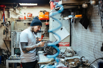 Side view portrait of modern tattooed man fixing broken  parts at table in  workshop