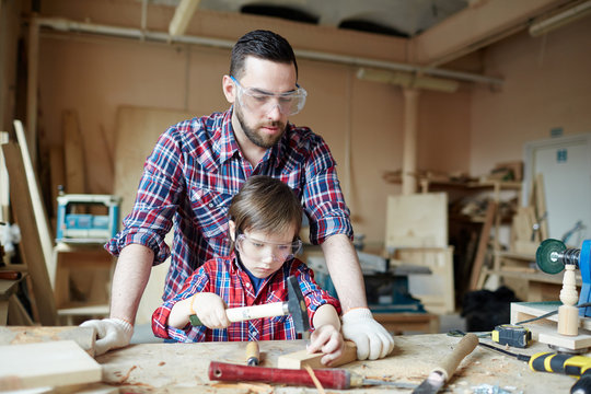 Young man looking at his son hammering nail in workshop
