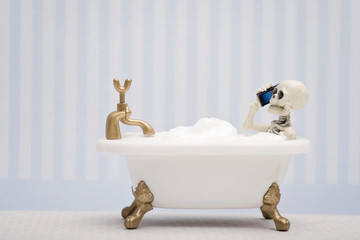 A skeleton talking on his cellphone while having bubble bath