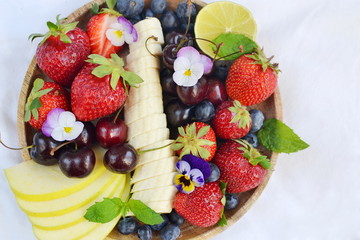 Wooden plate with fruits and berries, blueberries, strawberries, cherry, apple, banana, healthy breakfast