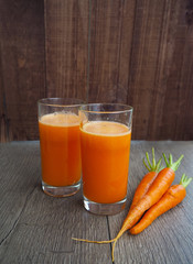 glass of fresh carrot juice with vegetables on wood background.