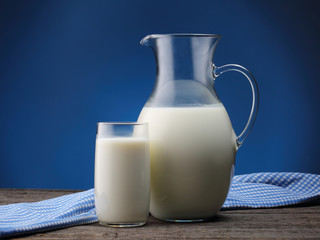 Pitcher and glass with some milk on blue