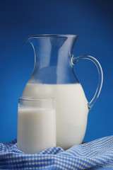 Pitcher and glass with some milk on blue