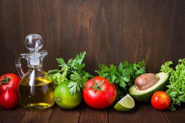 Fresh tomatoes, lime, avocado, lettuce, parsley and olive oil on dark wood background with space for text. Healthy food. Vegetables and greens. Salad ingredients.