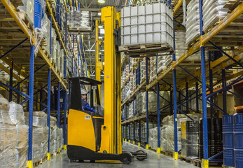 Warehouse worker on stacker loading cargo on rack