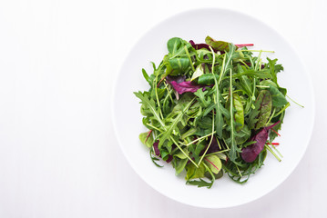 Fresh salad with mixed greens (arugula, mesclun, mache) on white wooden background top view. Healthy food.
