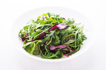 Fresh salad with mixed greens (arugula, mesclun, mache) on white wooden background close up. Healthy food.