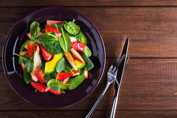Healthy salad plate with avocado, strawberry, chicken and spinach on wooden background top view. Food and health. Clean eating.