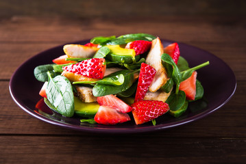 Healthy salad plate with avocado, strawberry, chicken and spinach on wooden background close up. Food and health. Clean eating.