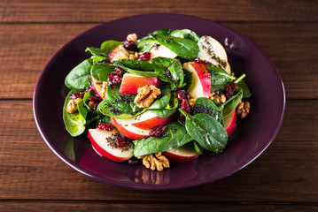 Healthy salad plate with apple, dried cranberry, walnut, spinach and poppy seed dressing on wooden background close up. Food and health. Clean eating.