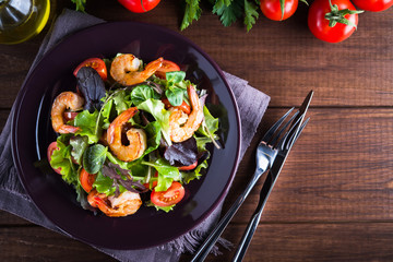 Fresh salad plate with shrimp, tomato and mixed greens (arugula, mesclun, mache) on wooden background top view. Healthy food. Clean eating.