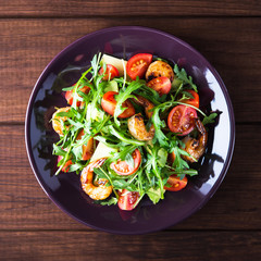 Fresh salad plate with shrimp, tomato, avocado and arugula (salad rocket) on wooden background top view. Healthy food. Clean eating.