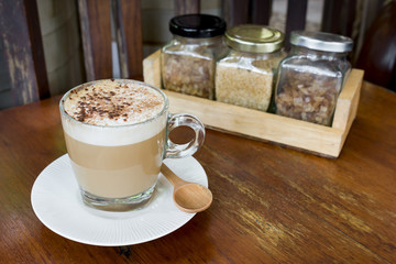 cup of capuccino coffee and three of sugar bottle on space of  old wood table at rustic coffee shop