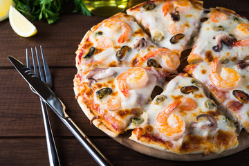 Sliced italian seafood pizza with shrimp, octopus, clams, mussels and squid on dark wooden background close up. Italian traditional food. Popular street food. Frutti di Mare pizza.