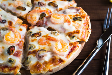 Sliced italian seafood pizza with shrimp, octopus, clams, mussels and squid on dark wooden background close up. Italian traditional food. Popular street food. Frutti di Mare pizza.