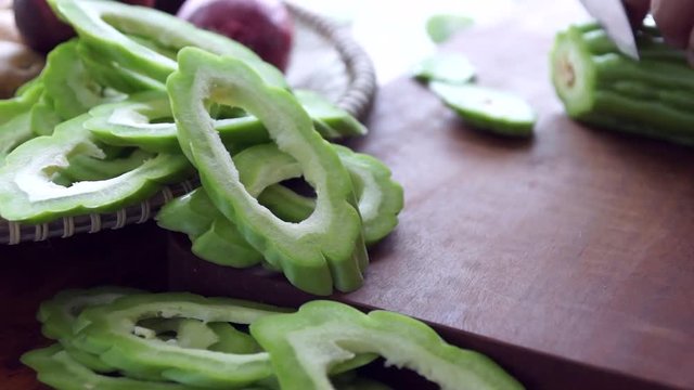 Out of focus view of cook's hands slicing bitter gourd with a Japanese gyuto