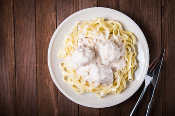 Pasta tagliatelle plate with meatballs and creamy sauce on dark wooden background top view. Italian cuisine. Delicious meal.