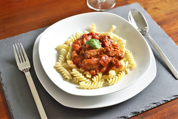 Delicious goulash dish on a white plate with basil leaf. Spiral pasta with tomato sauce.