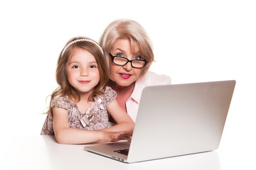 Grandmother and her granddaughter sitting at the table and using laptop on white background
