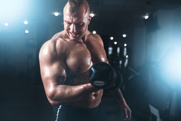 Fototapeta na wymiar Muscular athlete posing with dumbbell in sport gym