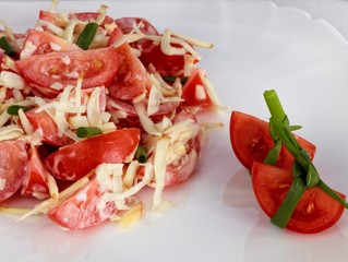 tomato salad with smoked cheese on the white plate with two tomato slices in front