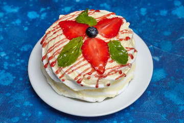 White creamy round cake with strawberries and mint on plate