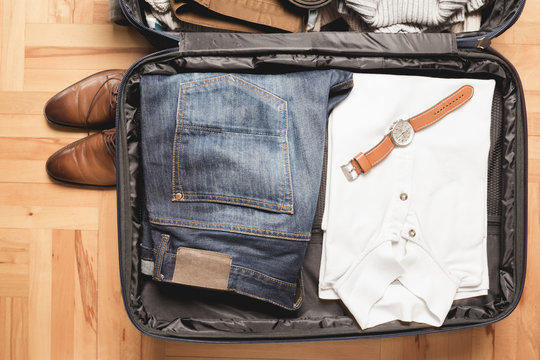 Open traveler's bag with men clothing, accessories, watch and belt. Travel and vacations concept. 